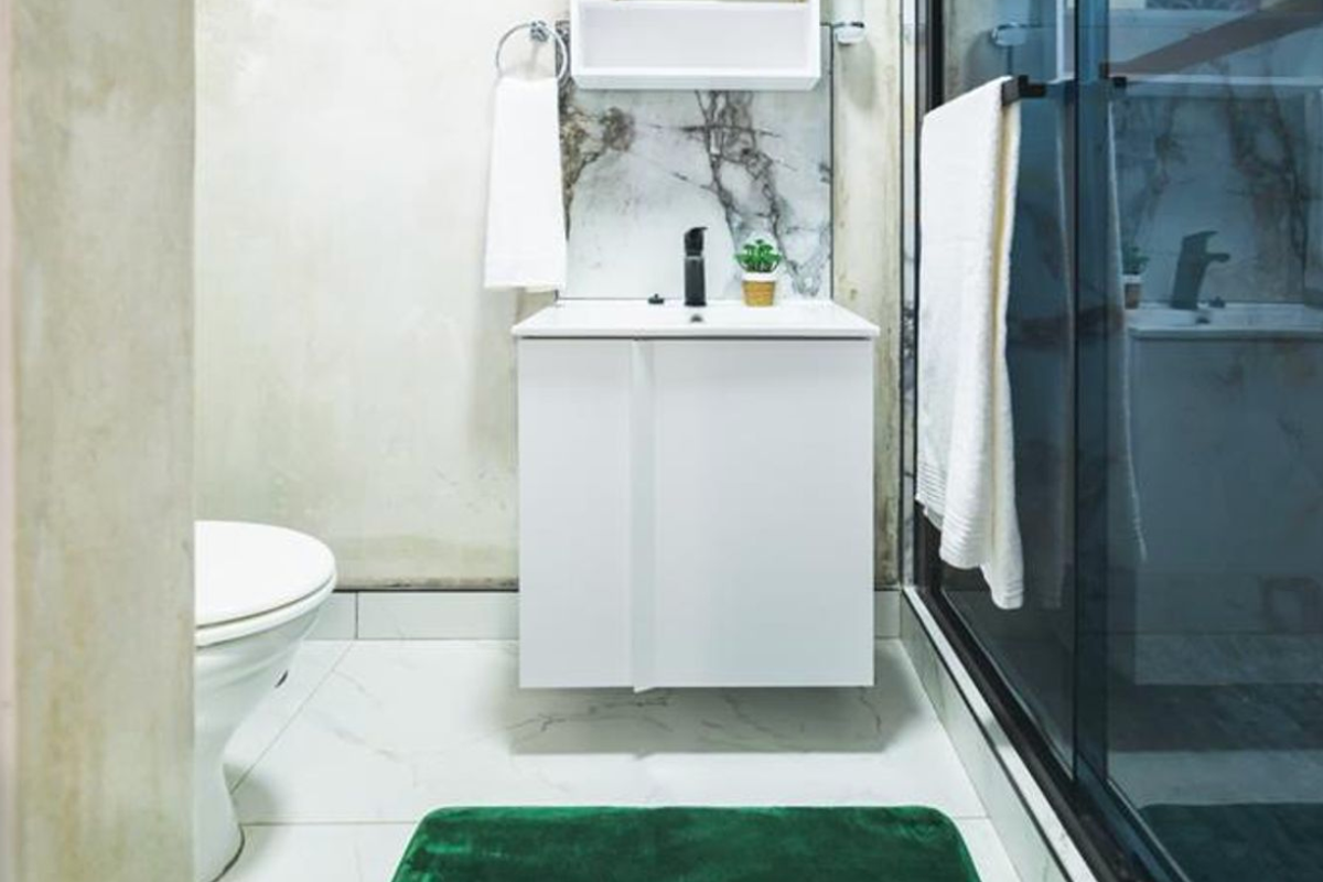 A compact bathroom featuring a modern white vanity with a black mixer tap, marble-look splashback, toilet, and a glass-enclosed shower.