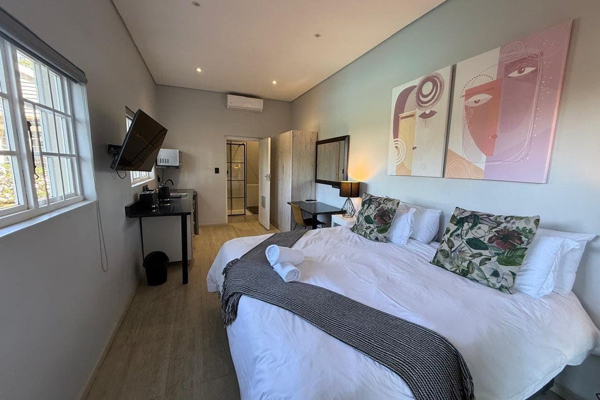 A well-maintained bedroom featuring wood-look flooring, recessed lighting, a wall-mounted air conditioning unit, and an en-suite bathroom access.