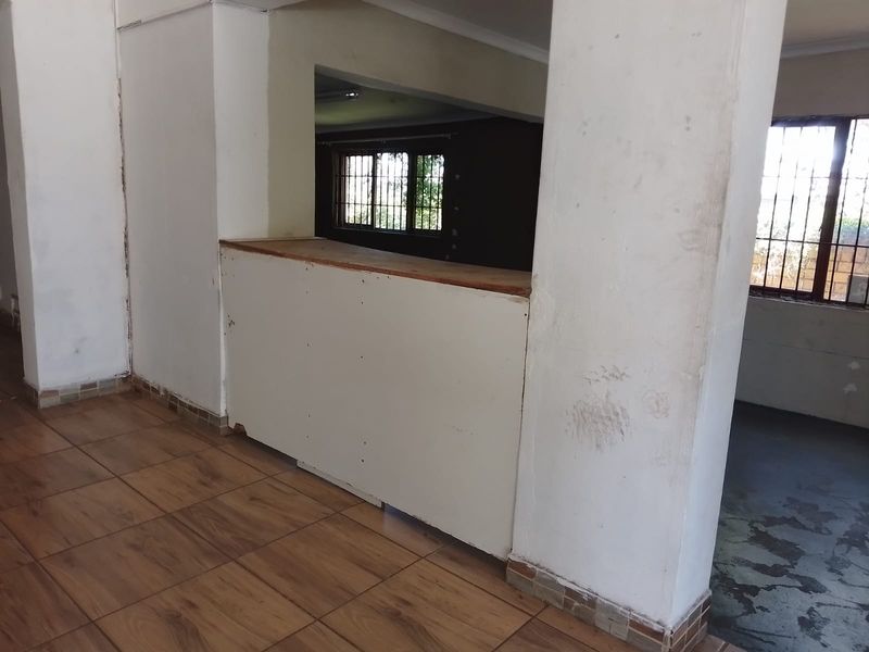 Open plan retail space featuring a built-in service counter, tiled flooring, and large windows with security bars, requiring cosmetic updates.