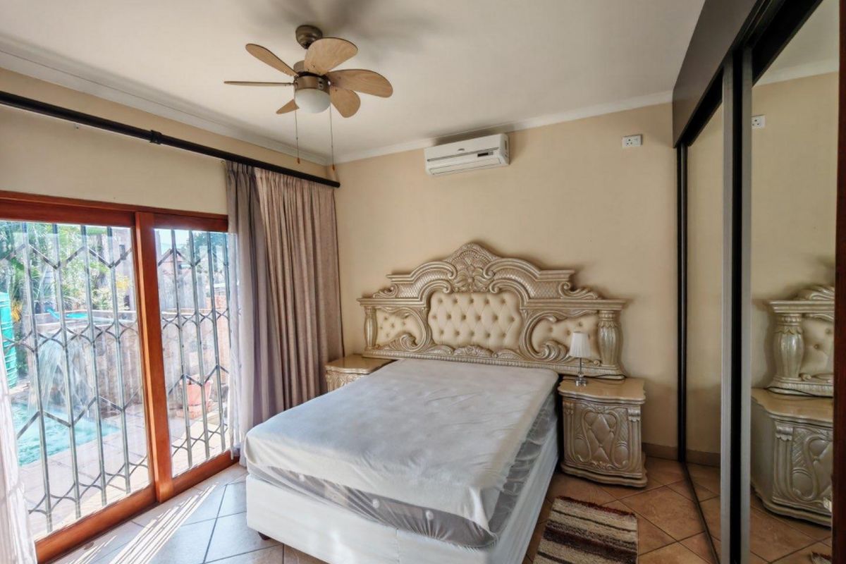 Bedroom featuring tiled flooring, a ceiling fan, wall-mounted air conditioning unit, and sliding glass doors with security gates leading to the exterior.