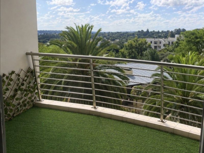 A private balcony featuring a stainless steel balustrade, tiled edging, and artificial grass flooring, offering an elevated view of the surrounding neighborhood.