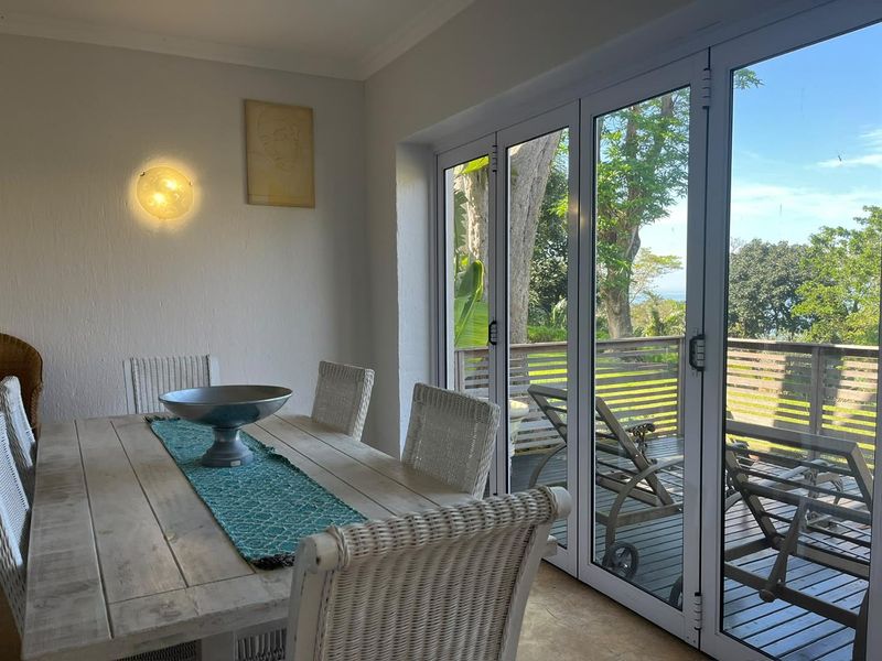 Bright dining area featuring large folding glass doors that open onto an outdoor deck, providing natural light and garden views.