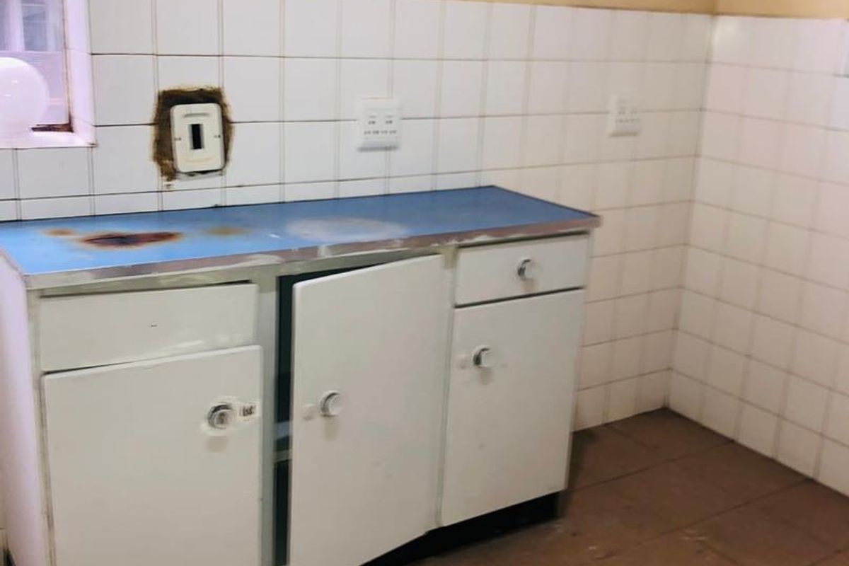 A dated kitchen area featuring basic built-in cabinetry, tiled backsplash, and worn countertop surfaces, requiring renovation to modernize the space.