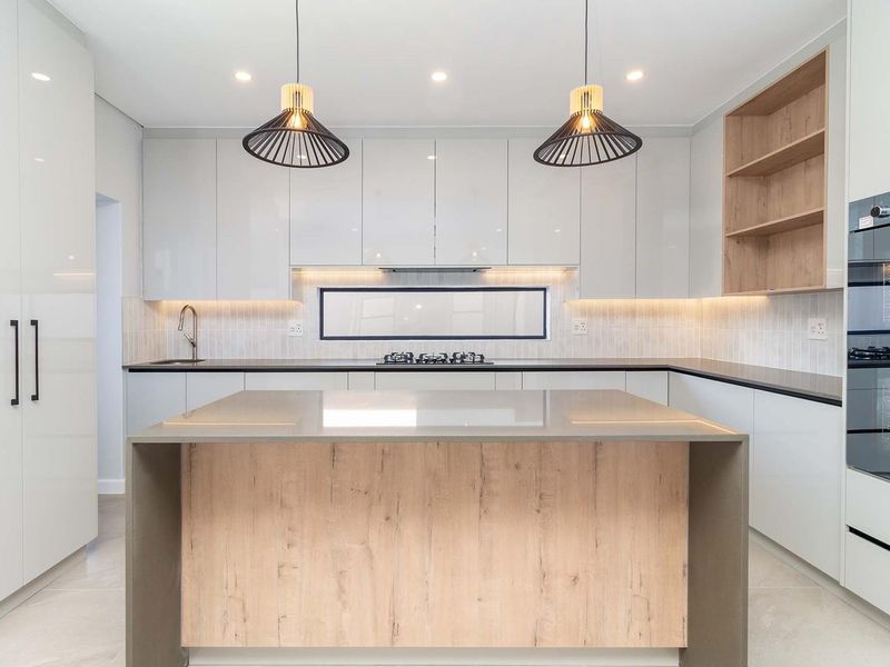 Modern kitchen featuring a central island, high-gloss cabinetry, built-in oven, gas cooktop, and integrated lighting with a clean, contemporary finish.