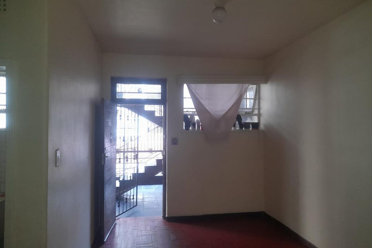 An empty living area featuring parquet flooring, a security gate at the entrance, and a window with metal burglar bars.