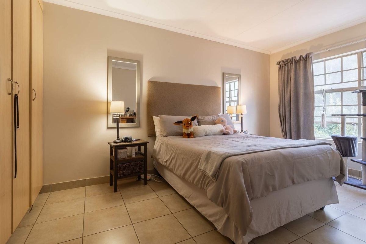A well-lit bedroom featuring neutral tiled flooring, built-in wooden cupboards, and a window with natural light.