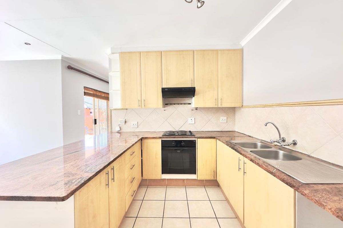 A functional kitchen featuring light wood cabinetry, granite countertops, built-in oven, electric hob, and a double stainless steel sink with tiled flooring.