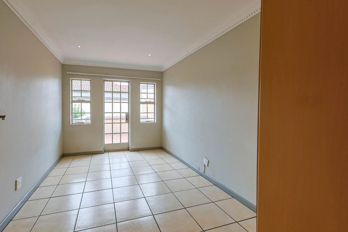 A bright, empty bedroom featuring neutral walls, tiled flooring, crown molding, and a glass-paneled door providing direct access to an outdoor area.