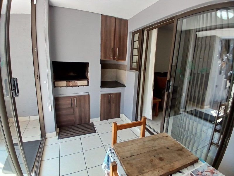 Covered balcony featuring a built-in braai, tiled flooring, and dark wood cabinetry, providing a functional outdoor entertainment space with sliding door access.