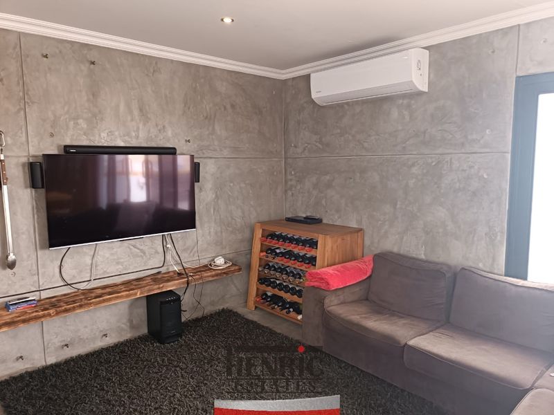A modern living room featuring industrial-style concrete panel walls, a split-system air conditioner, and a custom floating timber shelf.