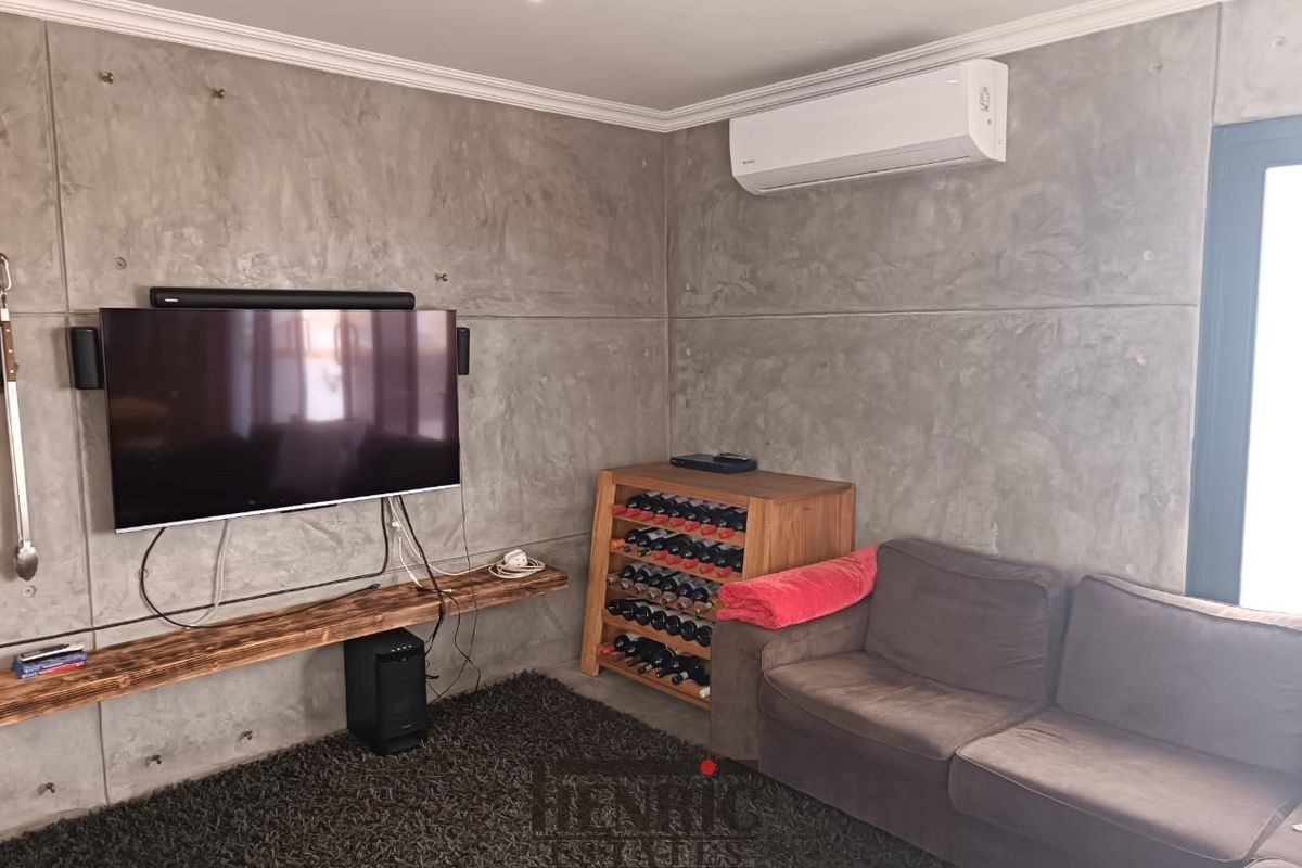 A modern living room featuring industrial-style concrete panel walls, a split-system air conditioner, and a custom floating timber shelf.
