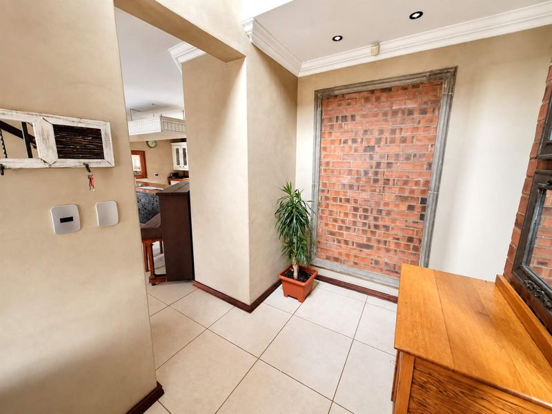 Welcoming entrance hall featuring a decorative exposed brick feature wall, neutral tiled flooring, and recessed ceiling lighting, leading through to the main living area.