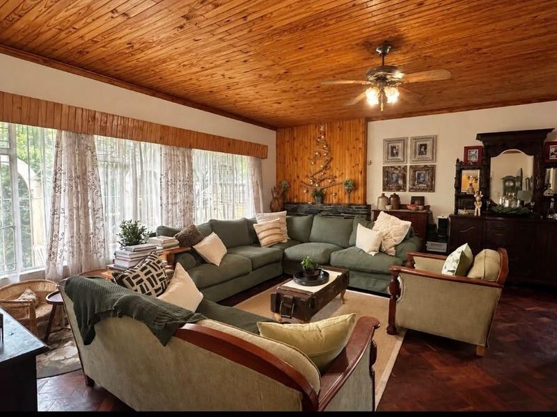 Spacious living room featuring warm timber ceiling and wall paneling, complemented by classic parquet flooring and large windows with security bars.