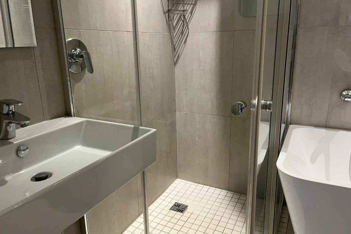Modern bathroom featuring a glass-enclosed shower, wall-mounted basin, and contemporary tiling throughout.