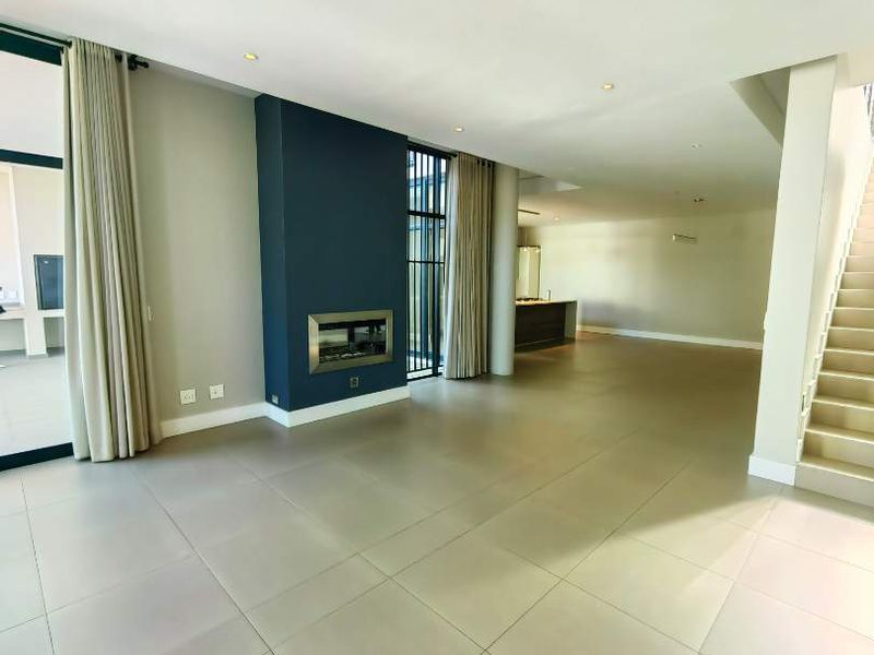 Spacious open-plan living area featuring large format floor tiles, a modern recessed fireplace, and a staircase leading to the upper level.
