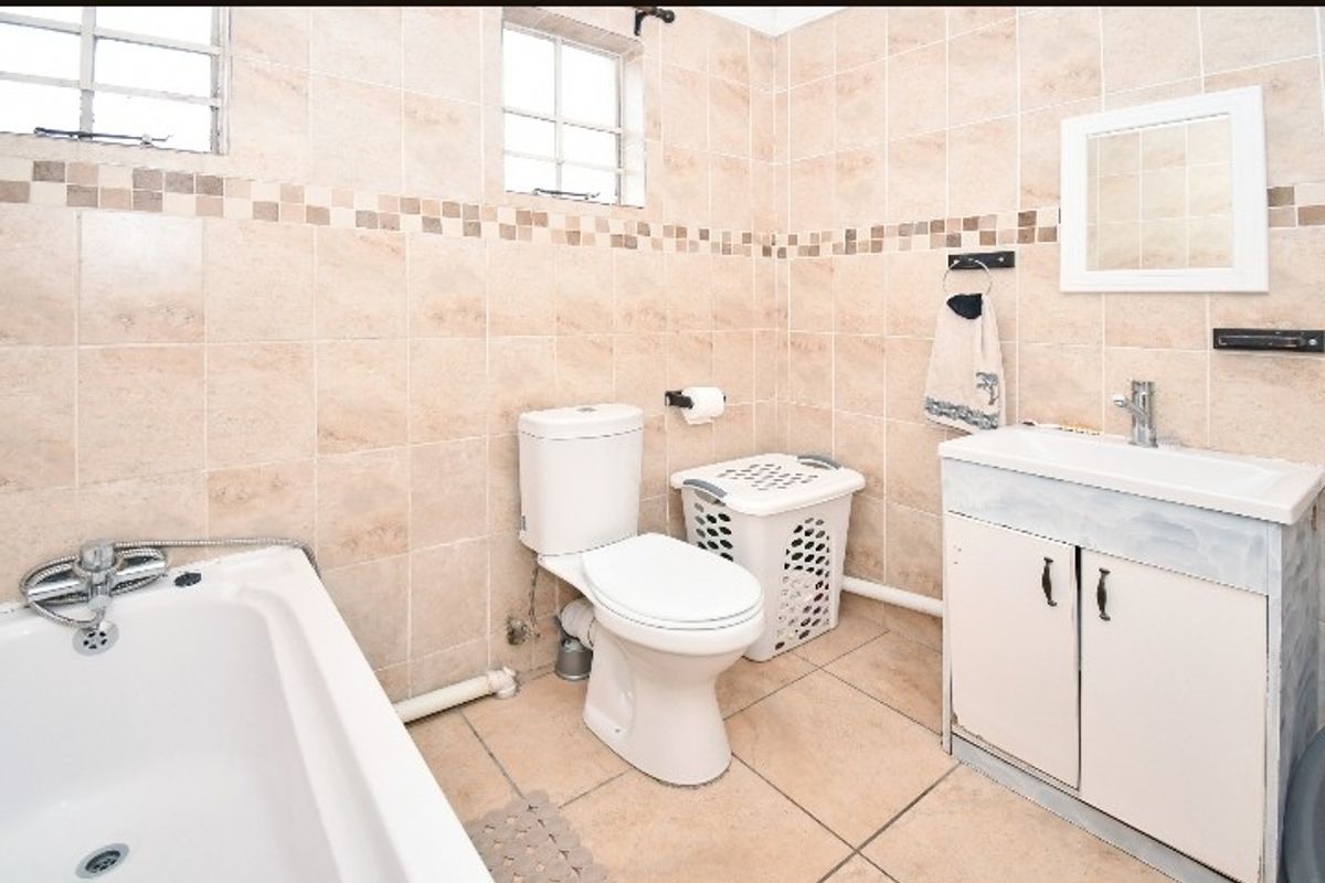 A functional bathroom featuring a bathtub, toilet, and vanity cabinet with tiled walls and flooring, offering a neutral base for potential cosmetic updates.