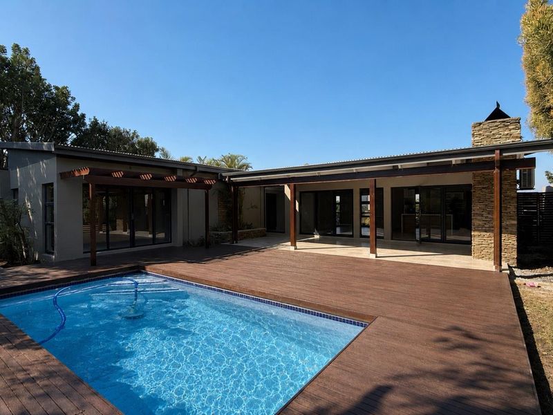 Spacious outdoor entertainment area featuring a swimming pool, extensive timber decking, and a covered patio with stone-clad chimney detail.