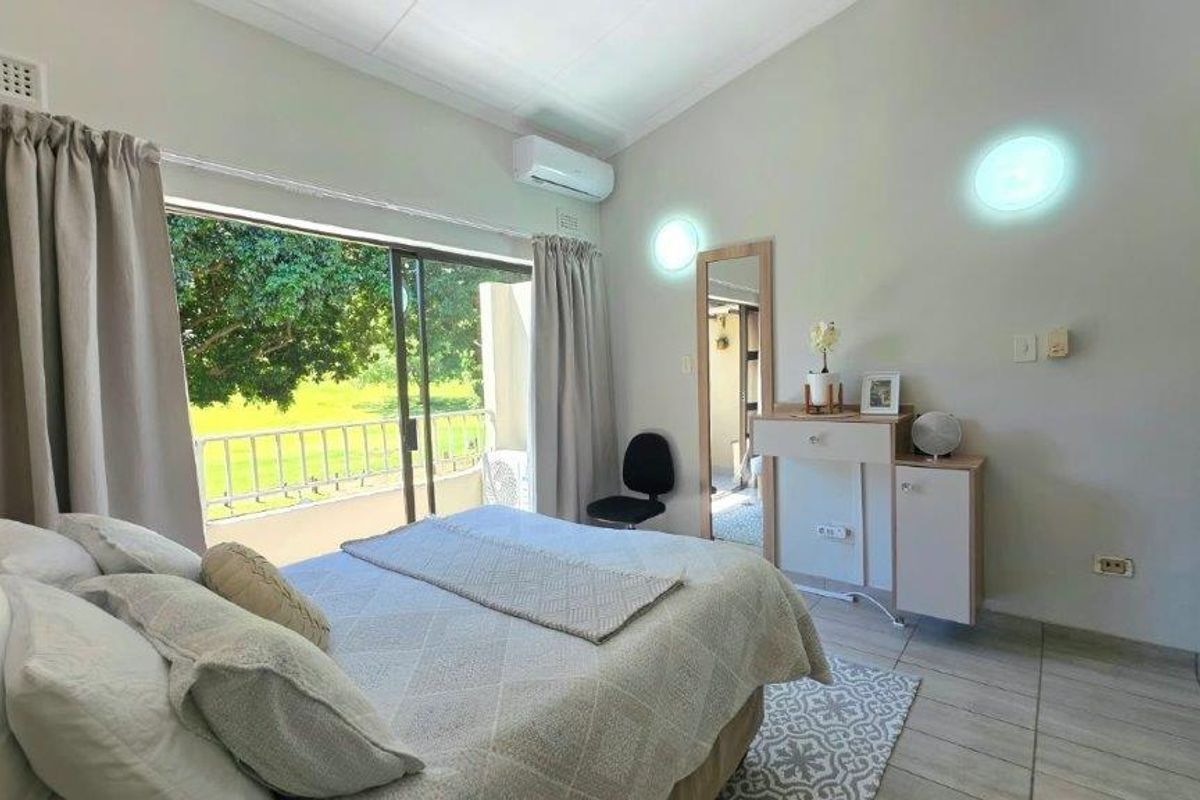 A bright bedroom featuring tiled flooring, a split-system air conditioner, and a large sliding glass door providing direct access to a private balcony.