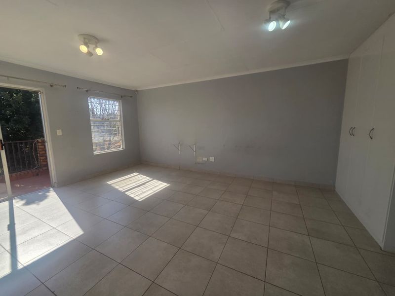 An empty bedroom featuring tiled flooring, built-in cupboards, and a sliding door providing access to an outdoor balcony area.