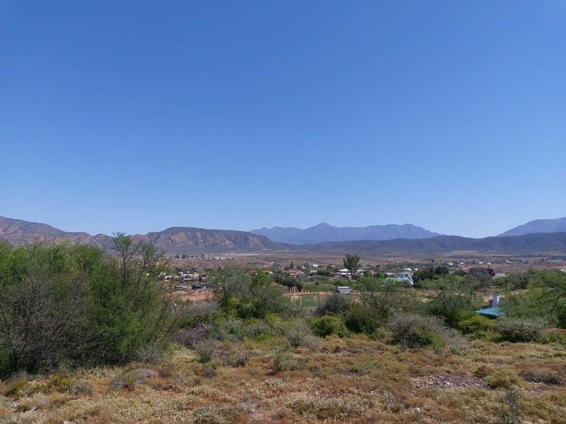A scenic landscape view overlooking a rural valley with distant mountain ranges under a clear blue sky.