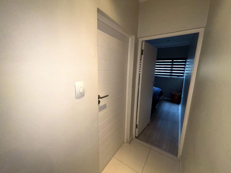 A clean, neutral hallway featuring tiled flooring and internal doors leading to adjacent rooms.