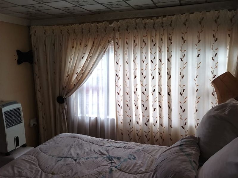 A bedroom featuring a patterned ceiling tile finish and window with curtains. The room requires maintenance to the ceiling and lighting fixtures.