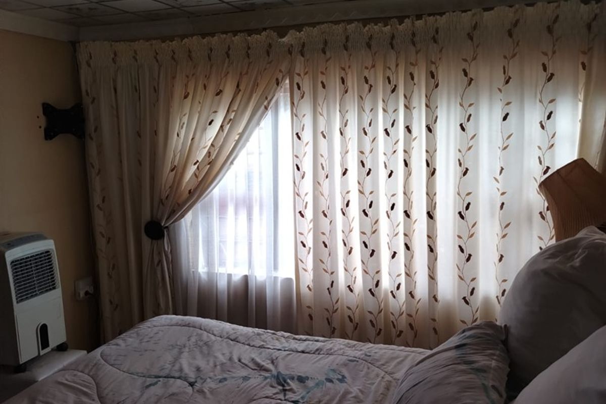 A bedroom featuring a patterned ceiling tile finish and window with curtains. The room requires maintenance to the ceiling and lighting fixtures.