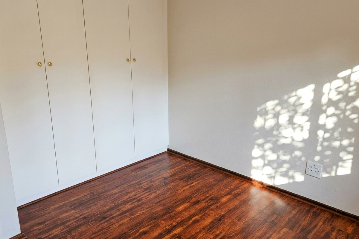 A bright, empty bedroom featuring dark laminate flooring and white built-in cupboards, offering a clean and neutral space ready for personalization.