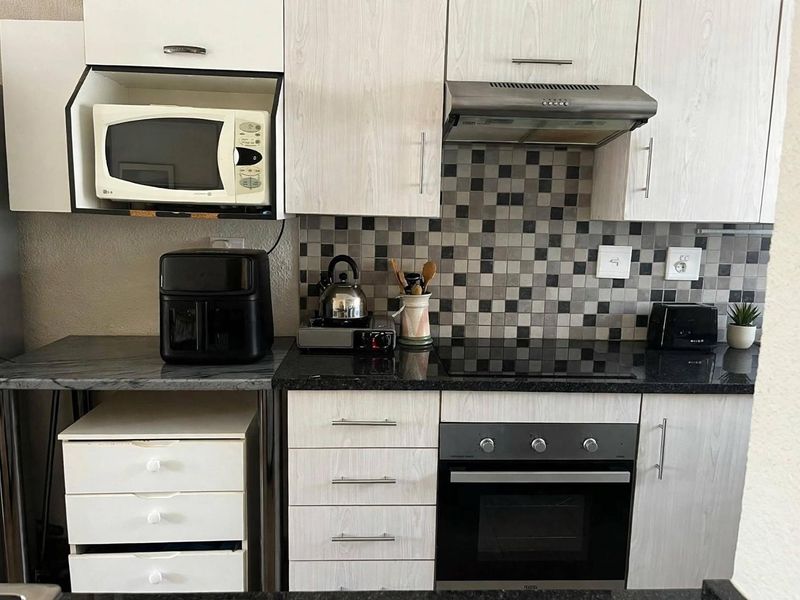 A functional kitchen featuring light wood-grain cabinetry, dark granite countertops, a mosaic tile backsplash, and integrated appliances including an oven, hob, and extractor fan.