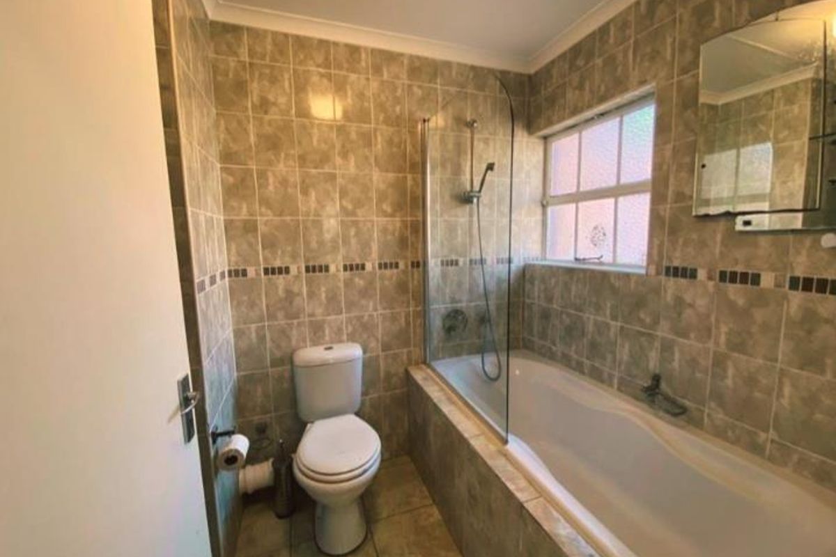 A functional bathroom featuring a bathtub with a glass shower screen, tiled walls and flooring, and a standard toilet.
