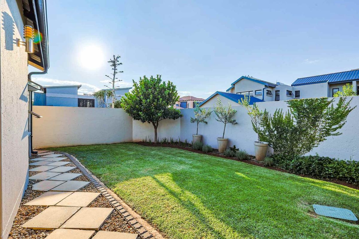 A well-maintained rear garden featuring a manicured lawn, paved walkway, and perimeter boundary walls.