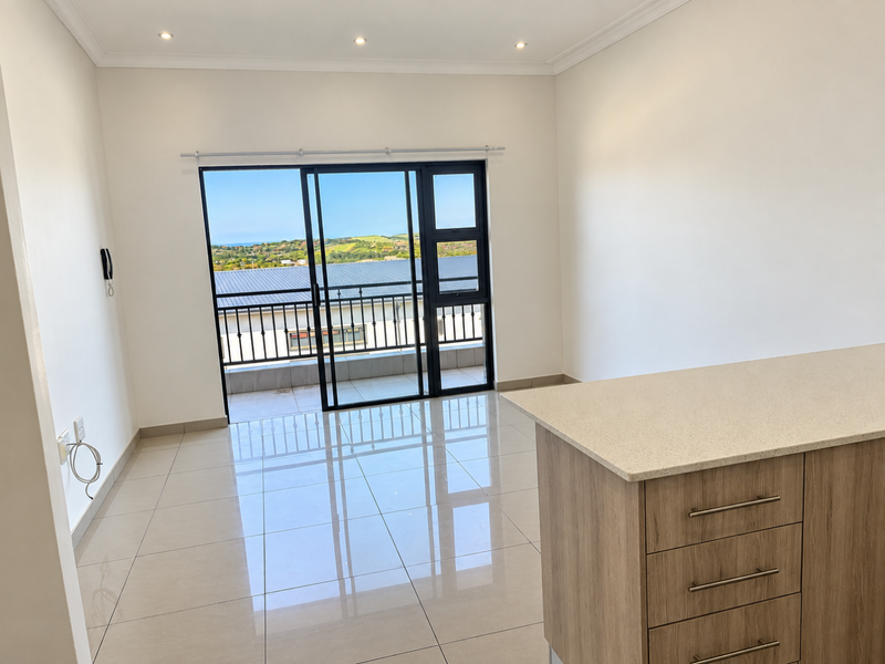 Bright open-plan living area featuring polished porcelain tiles, modern kitchen island with stone countertop, and sliding doors leading to a balcony with scenic views.