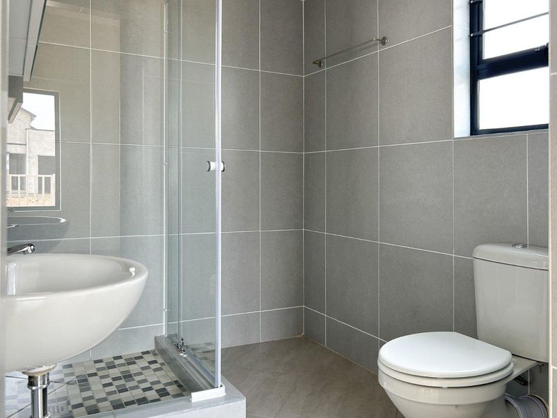 A modern, clean bathroom featuring grey wall tiles, a glass shower enclosure, a pedestal basin, and a standard toilet.