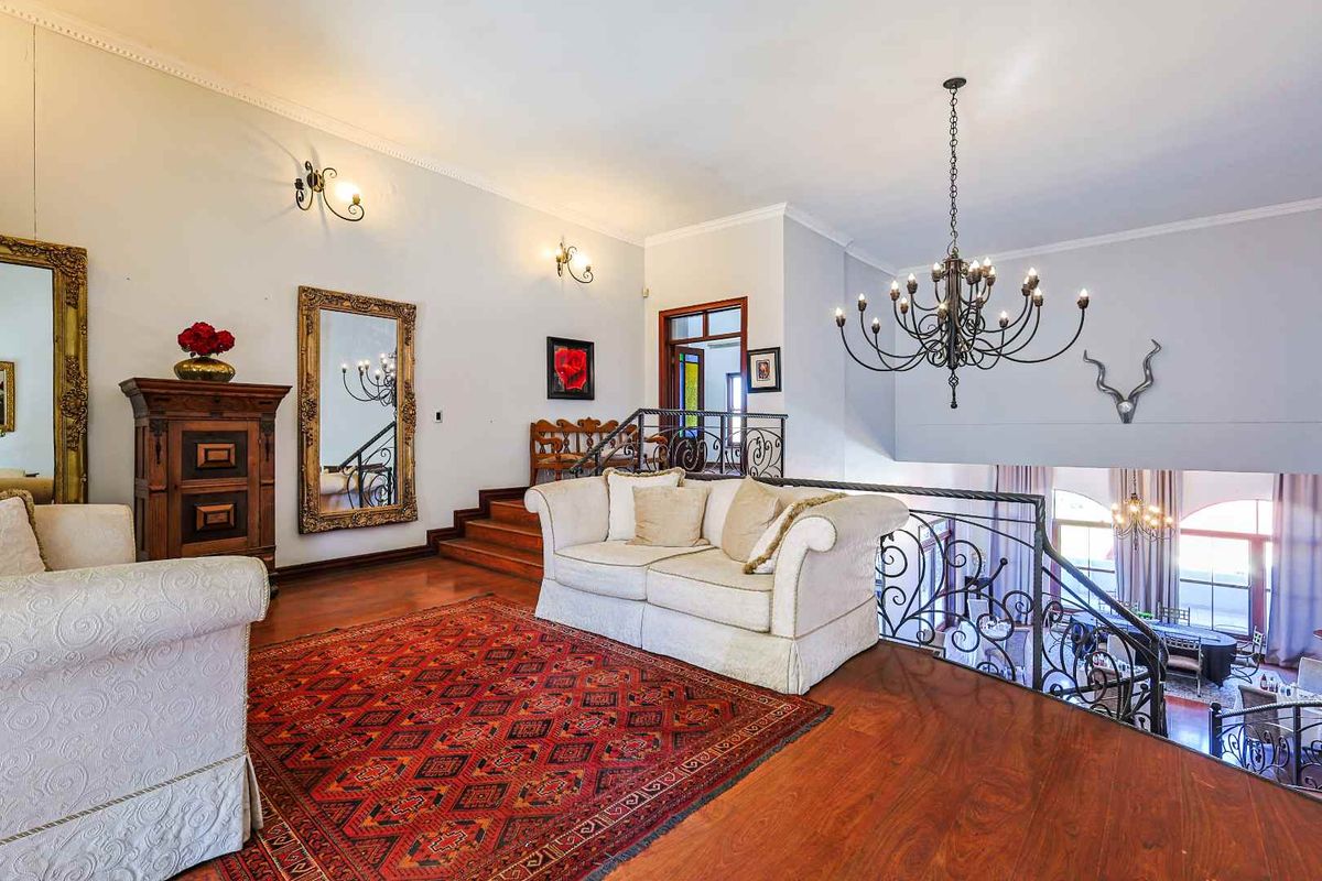 Spacious mezzanine living area featuring polished hardwood flooring, ornate wrought iron balustrades, and a grand chandelier overlooking the lower level.