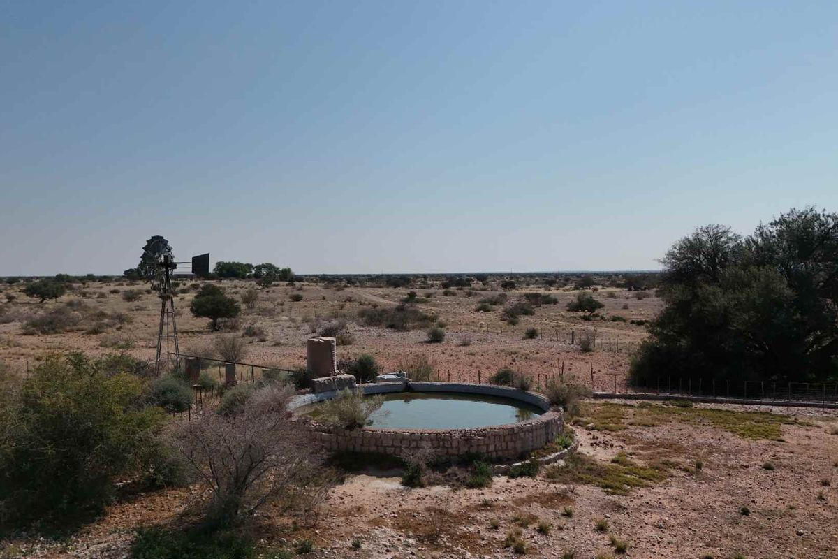 Aerial view of a farm landscape featuring a traditional windmill and a circular stone-walled water reservoir.