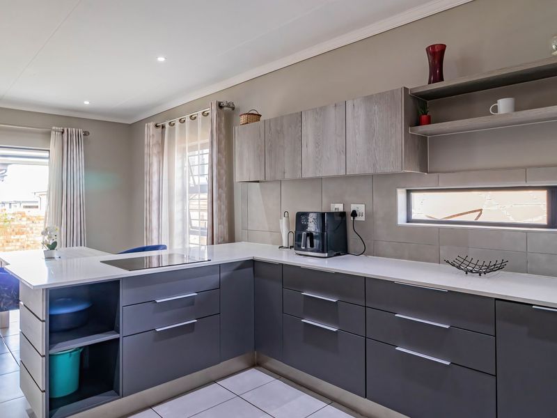 Modern kitchen featuring sleek grey cabinetry, stone countertops, an integrated electric cooktop, and a neutral tiled backsplash with recessed lighting.