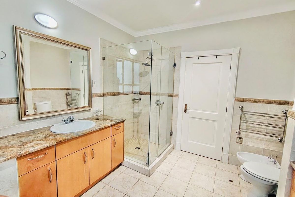 A well-maintained bathroom featuring a granite-topped vanity, glass-enclosed shower, bidet, toilet, and a heated towel rail with neutral tiled finishes.