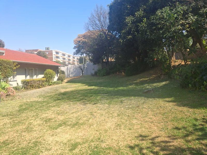 A spacious, established garden area featuring a large lawn, mature trees, and a boundary wall, adjacent to the side of the house.