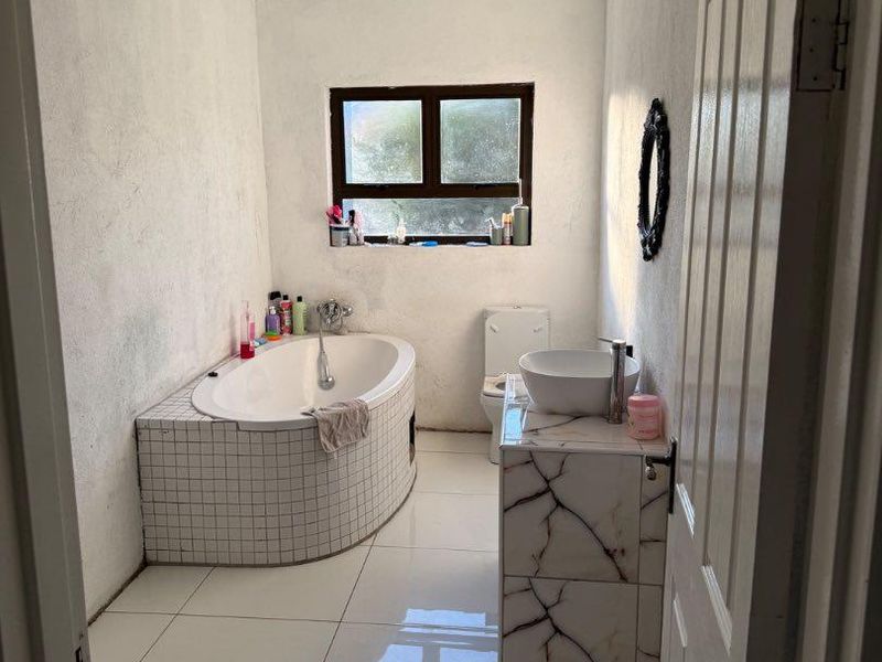 A functional bathroom featuring a built-in bathtub, a marble-look tiled vanity with a vessel sink, and white floor tiles.