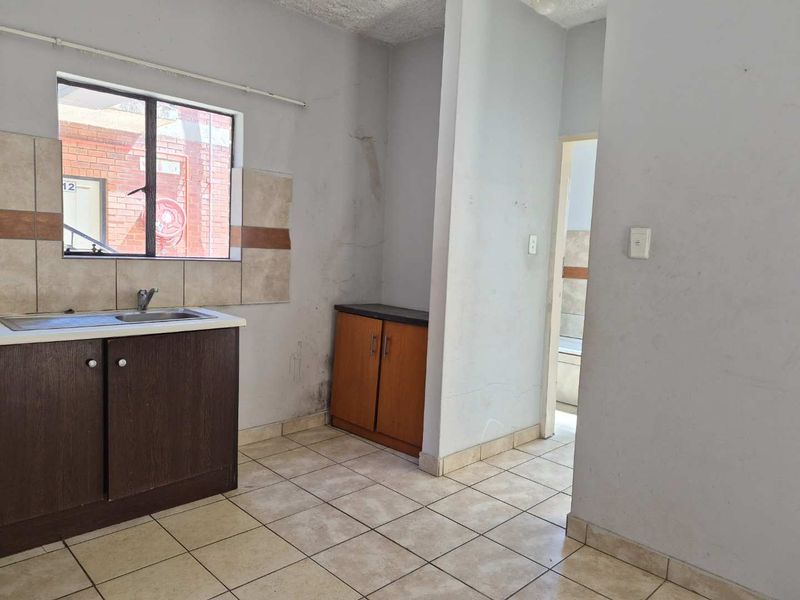 A compact kitchen area featuring tiled flooring, a single sink unit, and built-in base cabinetry, requiring cosmetic updates and wall repairs.