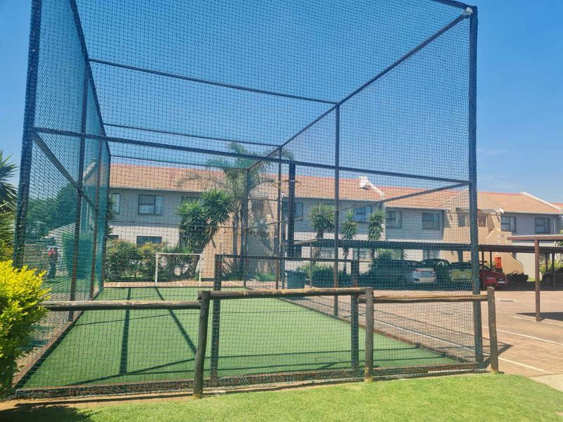 A well-maintained outdoor sports cage featuring synthetic turf flooring and secure perimeter fencing, located within the apartment complex grounds.
