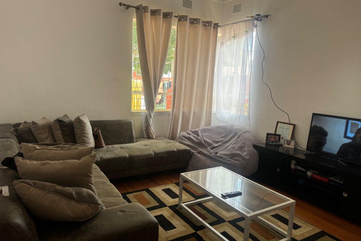 A living room featuring hardwood flooring and corner windows with curtain rods.