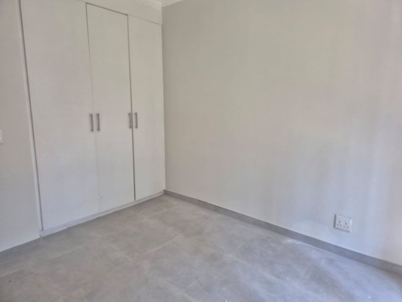 A clean, empty bedroom featuring neutral tiled flooring and built-in white cupboards, providing a versatile space ready for personalization.