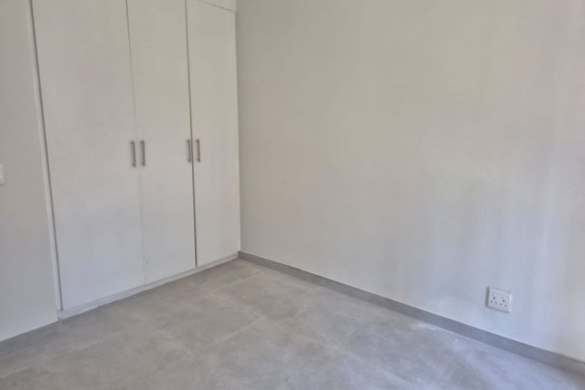 A clean, empty bedroom featuring neutral tiled flooring and built-in white cupboards, providing a versatile space ready for personalization.