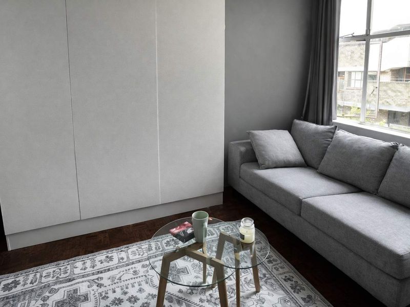 A living room featuring dark parquet flooring, neutral grey walls, and extensive built-in cabinetry providing ample storage space.