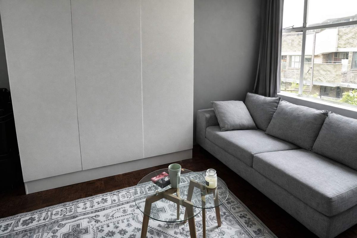 A living room featuring dark parquet flooring, neutral grey walls, and extensive built-in cabinetry providing ample storage space.