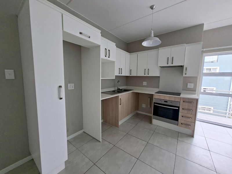 Modern kitchen featuring white and wood-tone cabinetry, integrated electric oven and hob, stainless steel sink, and neutral tiled flooring.