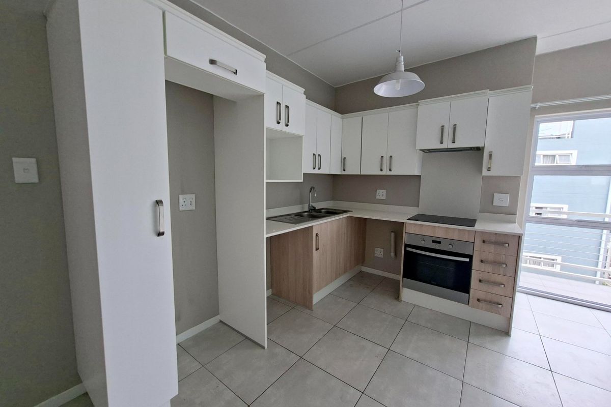 Modern kitchen featuring white and wood-tone cabinetry, integrated electric oven and hob, stainless steel sink, and neutral tiled flooring.