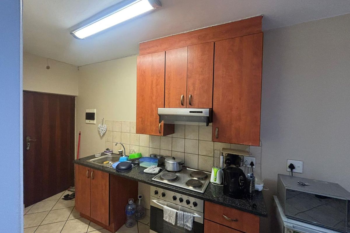 A functional kitchen featuring wood-finish cabinetry, a built-in oven with hob, extractor fan, and a tiled backsplash with a stainless steel sink.