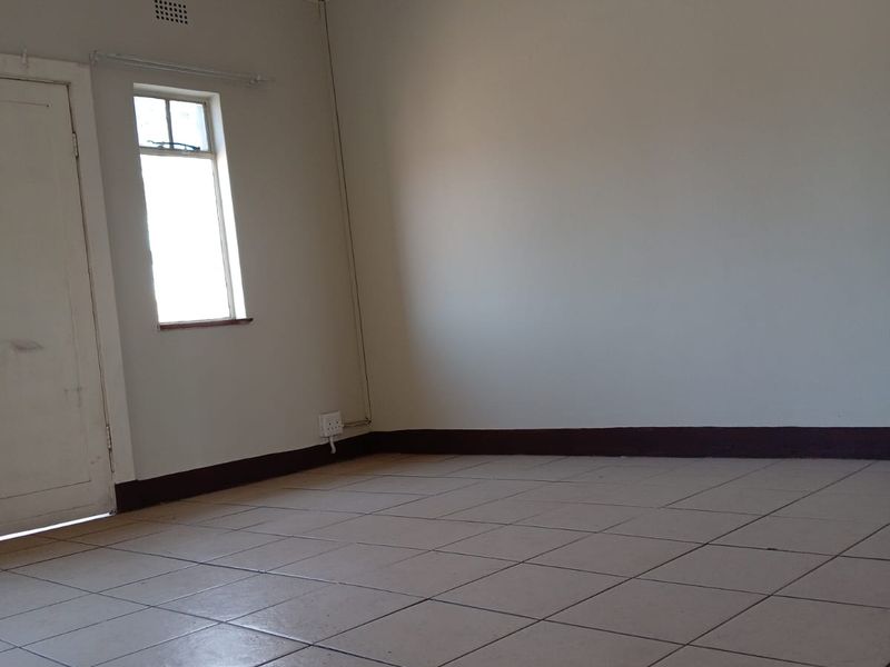 An empty living room featuring tiled flooring, decorative pressed metal ceilings, and traditional cornice detailing, awaiting renovation or staging.